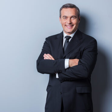 Successful businessman. Portrait of confident mature man in formalwear looking at camera and smiling while keeping arms crossed and standing against grey background